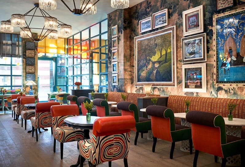 The Orangery at Warren Street Hotel featuring a backlit wall of orange niches filled with ceramic pots, woven bistro chairs, and maximalist colorful decor.