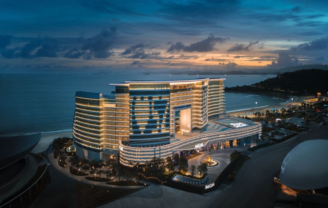 MGM Shenzhen's undulating S-curve facade illuminated at twilight against the Xiaomeisha coastline.
