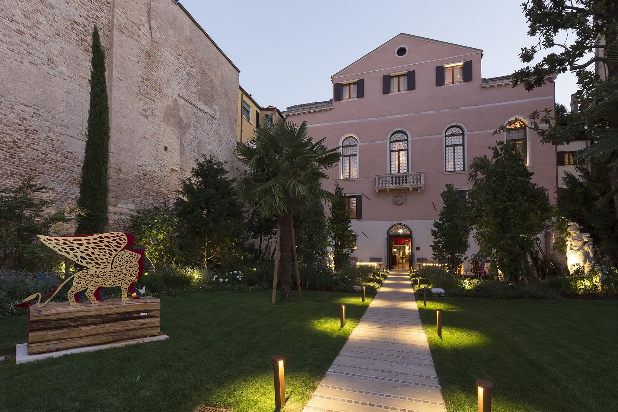 A serene private garden with magnolia trees leading to a wrought-iron gate that opens directly onto the Grand Canal in Venice.