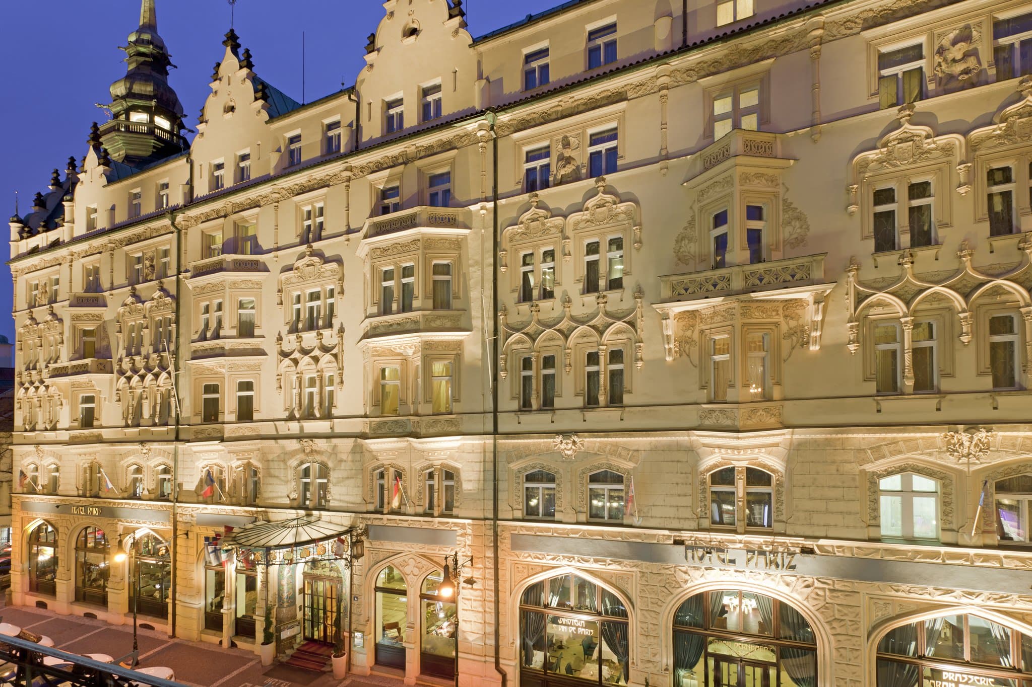 The grand interior of the Sarah Bernhardt Restaurant at Hotel Paris Prague featuring blue ceramic mosaics, gold stucco details, and large arched windows.