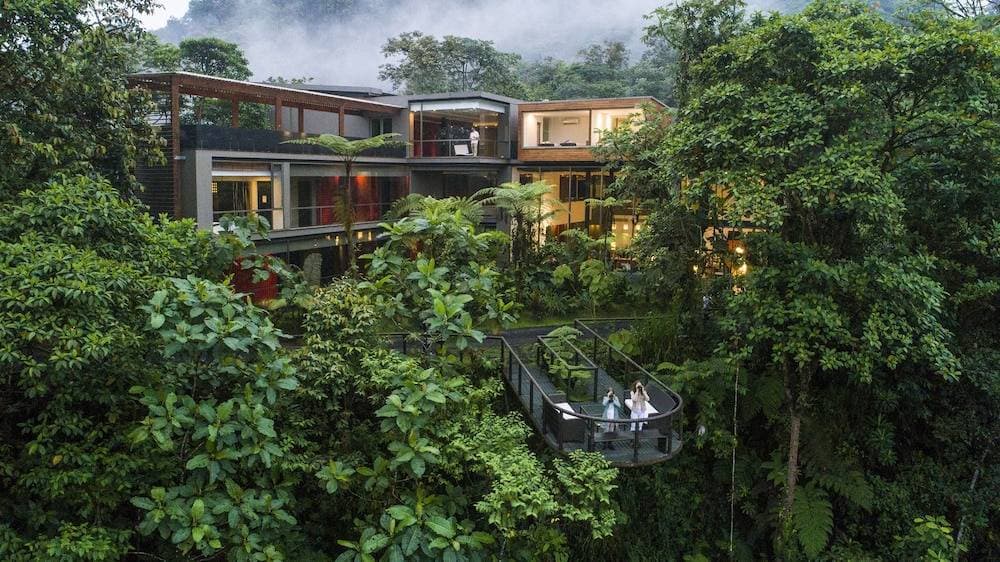 Mashpi Lodge's glass-walled structure glowing warmly at twilight amidst the dense, misty Chocó cloud forest.