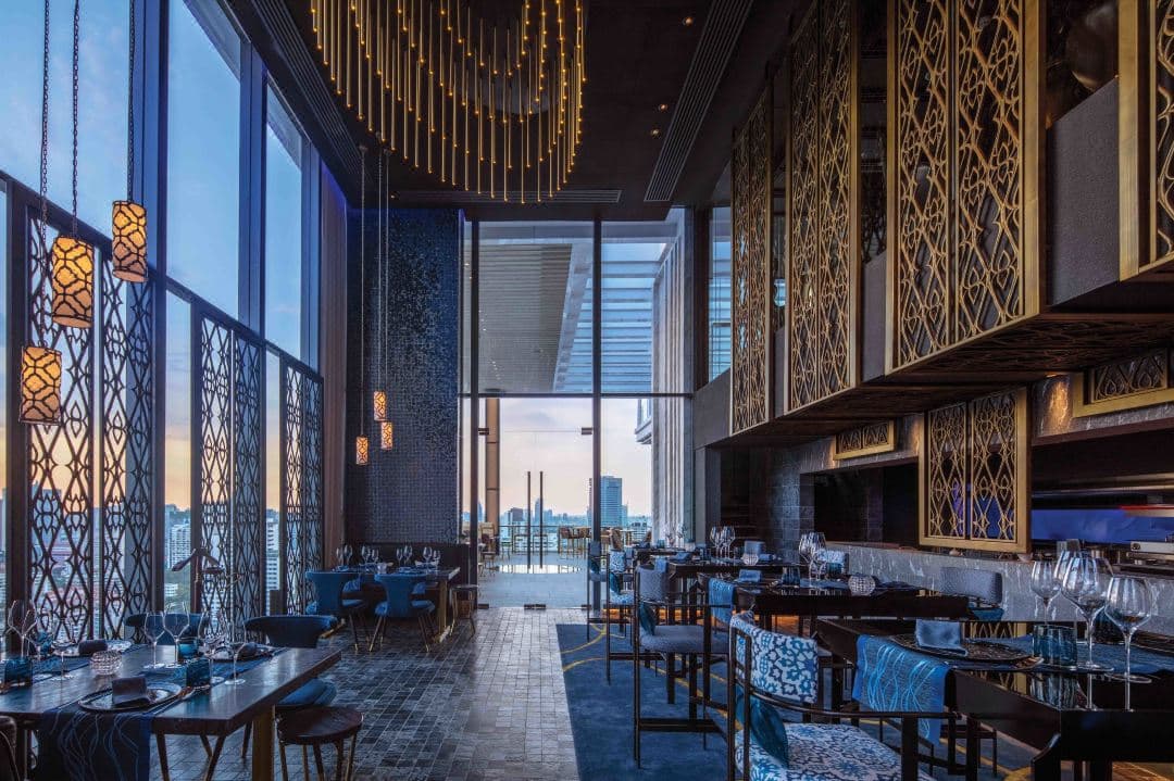 A sleek, expansive infinity pool on the 27th floor of 137 Pillars Residences Bangkok overlooking the city skyline at dusk.