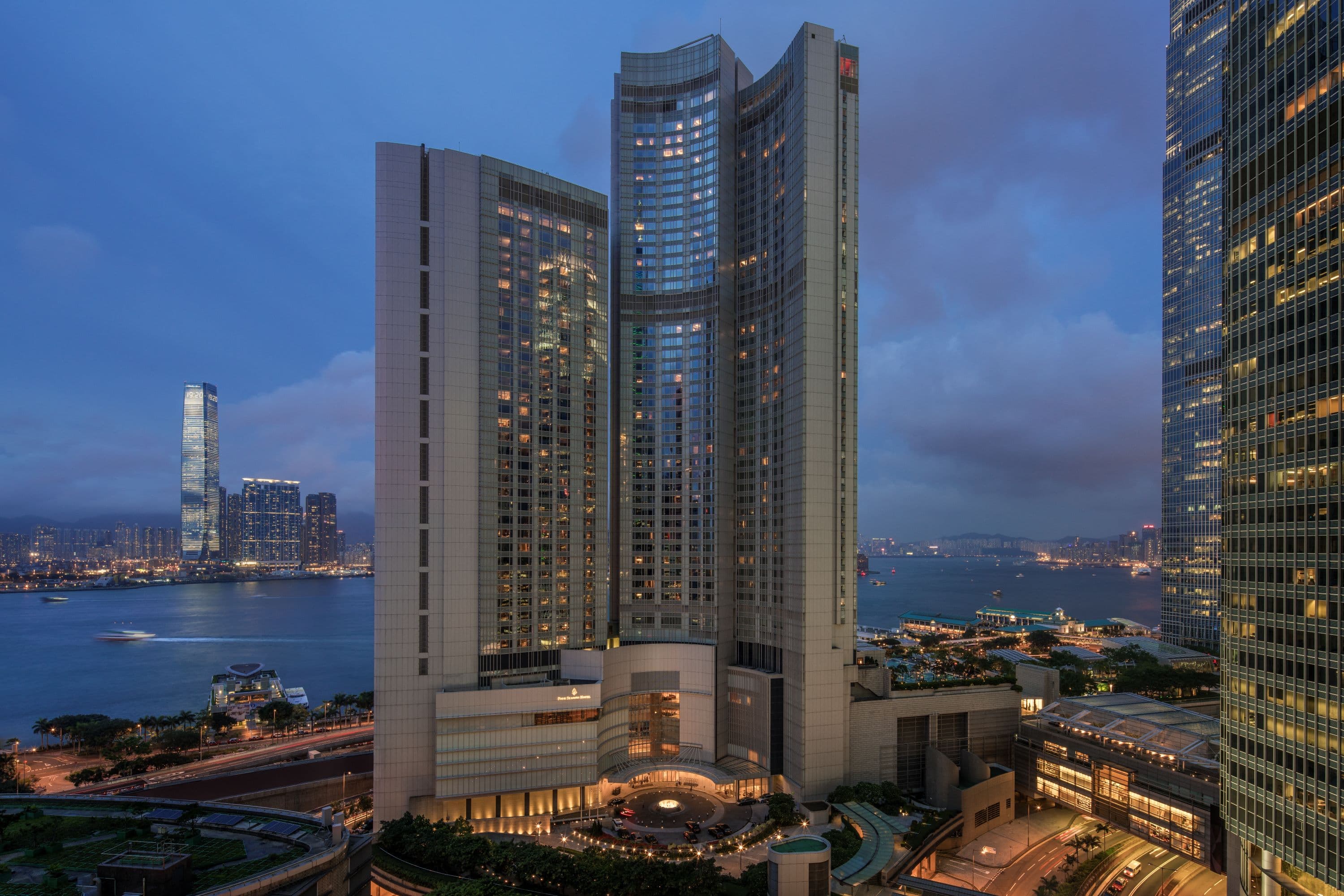 A dramatic dusk shot of the Four Seasons Hong Kong infinity pool merging with Victoria Harbour, with the illuminated skyline in the background.