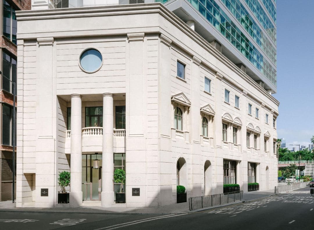 Lanson Place Causeway Bay facade featuring 19th-century French stone architecture and grand columns, illuminated warmly at dusk.