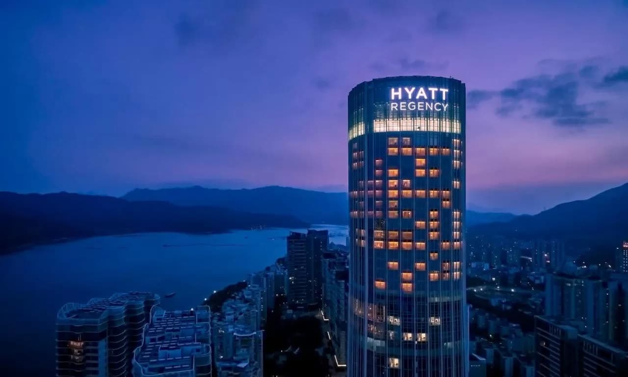 A woman swimming in the heated outdoor infinity pool at Hyatt Regency Shenzhen Yantian with the city skyline and mountains in the background.