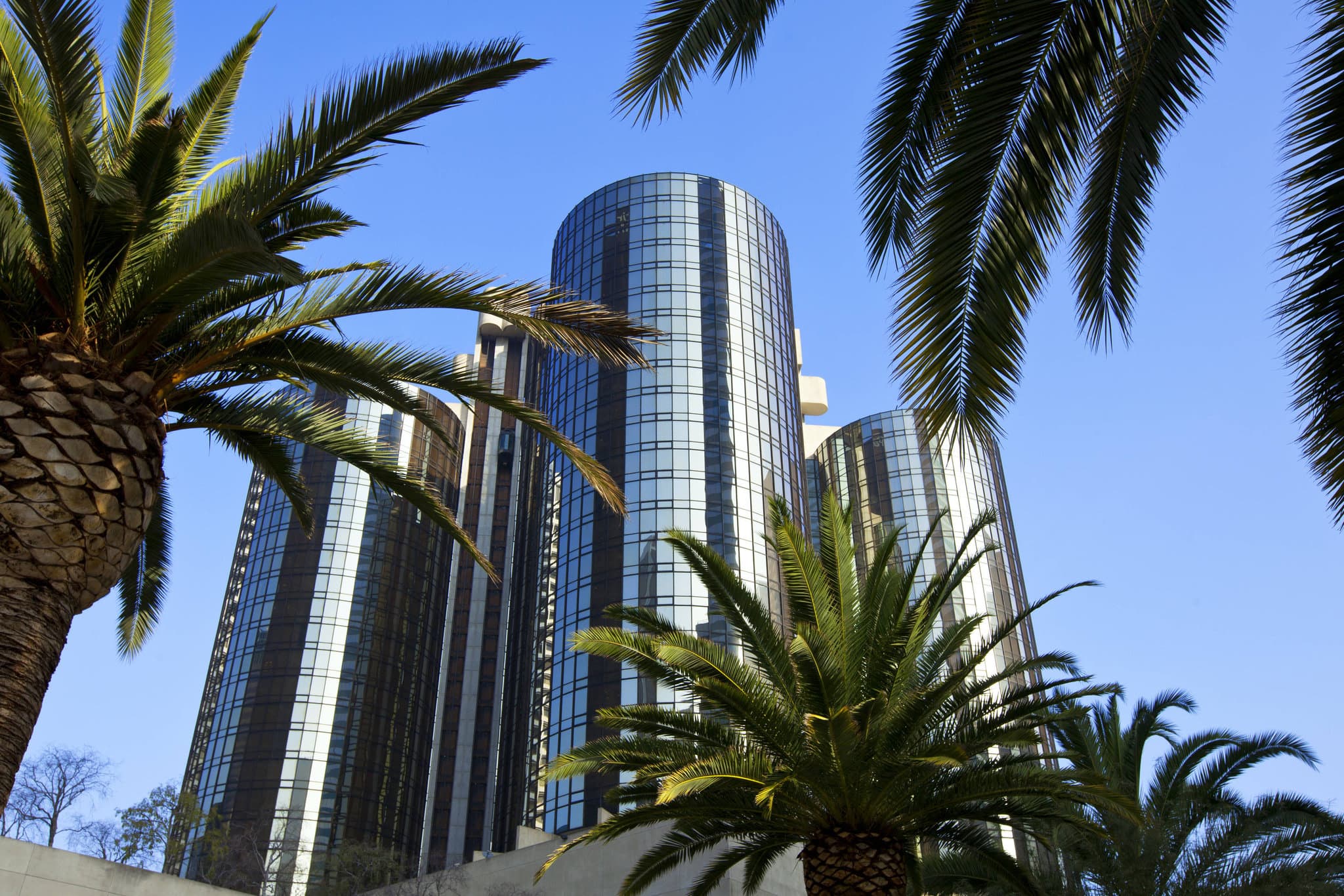 Looking up at the Westin Bonaventure's cylindrical glass towers and concrete skybridges against a blue Los Angeles sky.