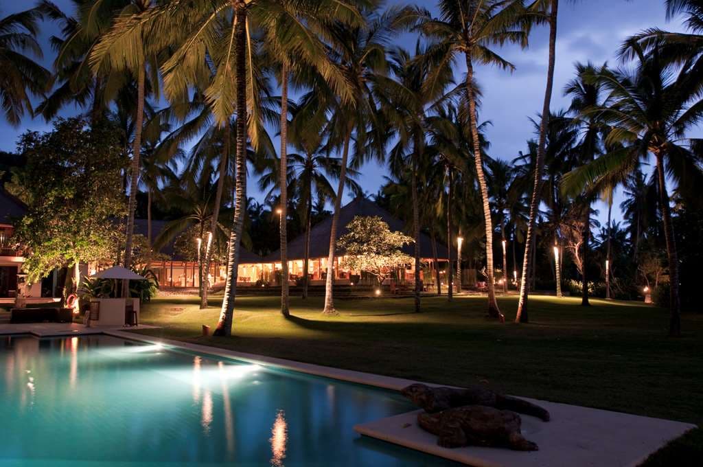 The iconic inverted pyramid pool at Alila Manggis surrounded by coconut palms and thatched-roof architecture.