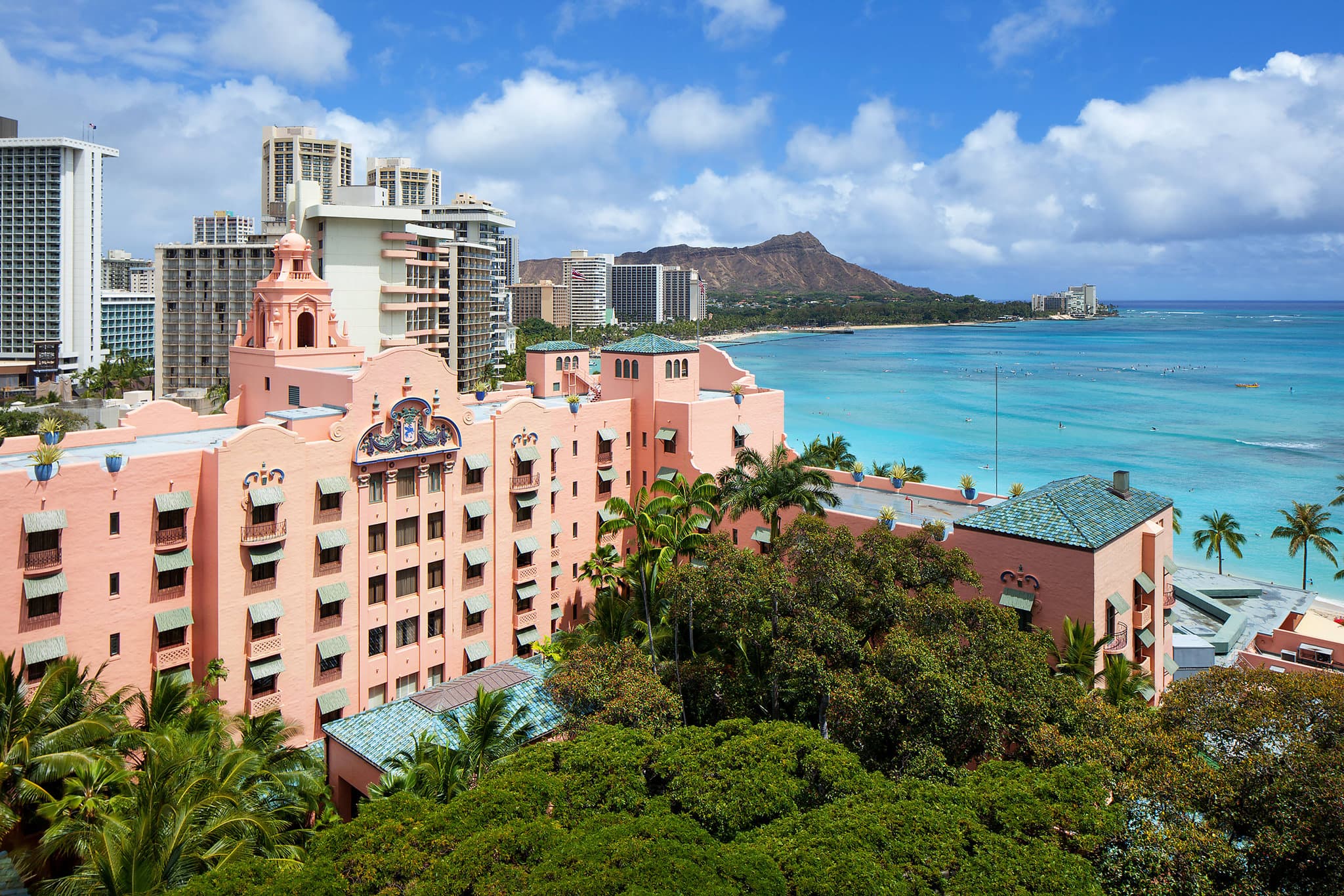The Royal Hawaiian's Spanish-Moorish pink facade glowing at sunset, framed by palm trees and the azure Waikiki ocean.