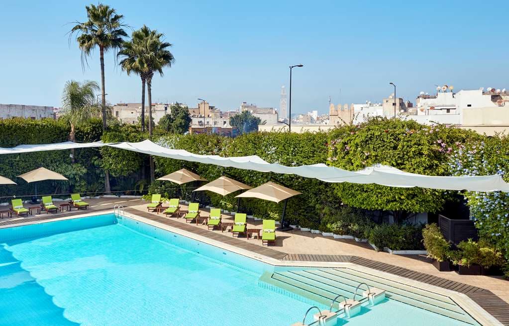 The Hyatt Regency Casablanca outdoor pool deck framed by palm trees with the white city skyline in the background.