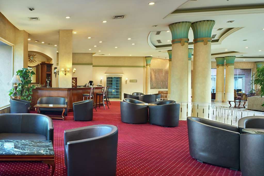 A sprawling indoor pool deck at Hilton Alexandria Green Plaza featuring lounge chairs and high glass ceilings.