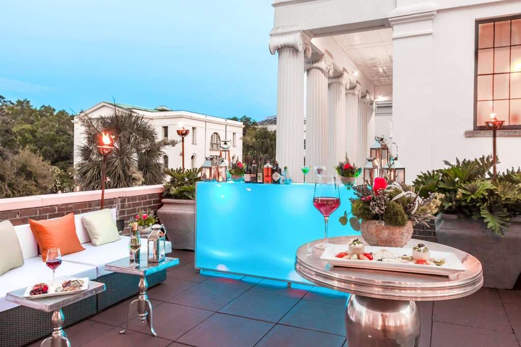 The Mills House Charleston exterior featuring its iconic pink façade, wrought iron balconies, and gas lanterns at twilight.