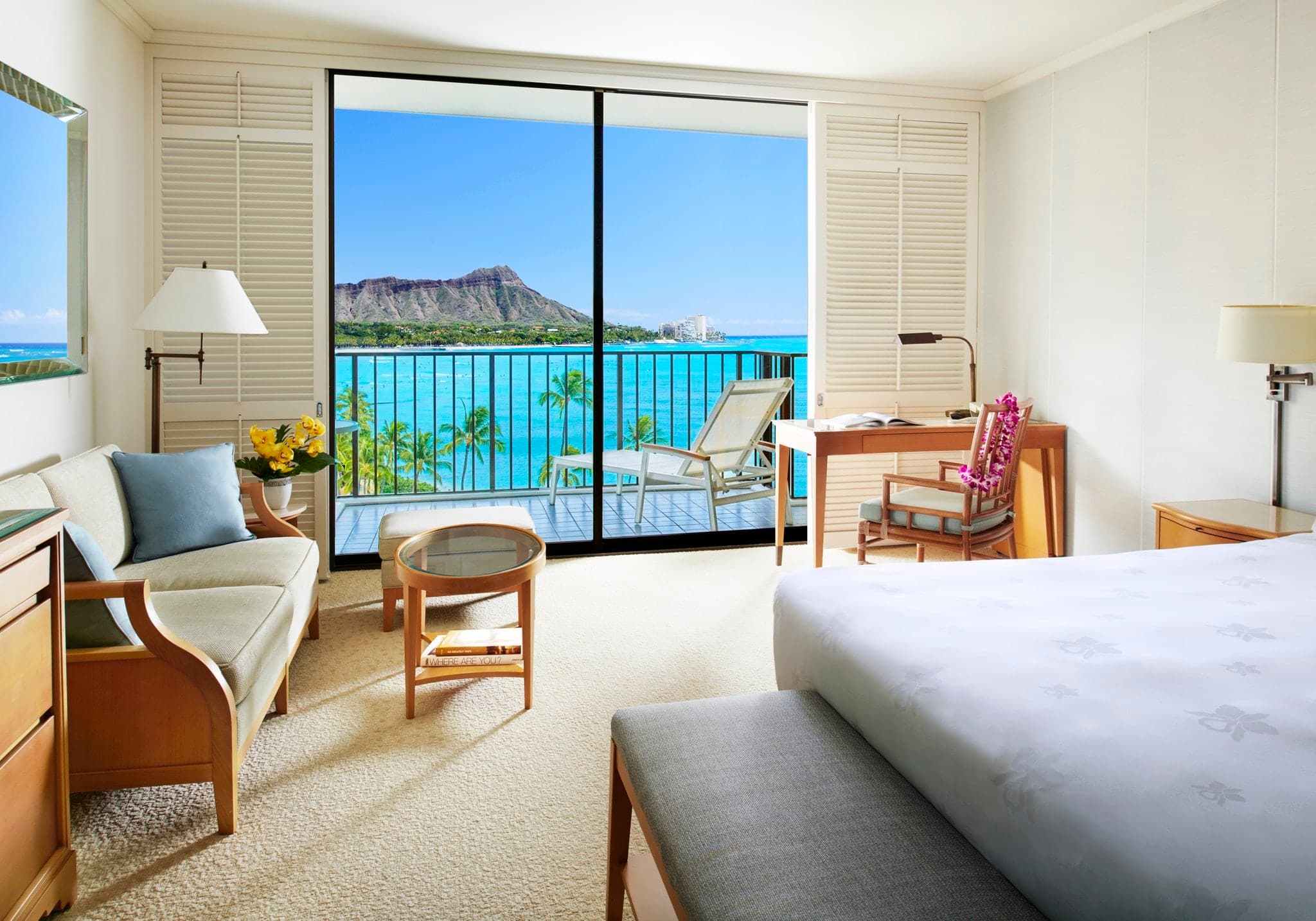 Aerial view of Halekulani's iconic oval pool featuring a 1.2 million glass tile orchid mosaic, surrounded by white loungers and the Waikiki coastline.