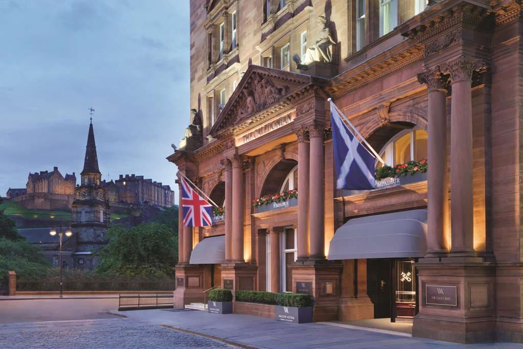 The Caledonian Edinburgh's red sandstone exterior glowing at dusk with the illuminated Edinburgh Castle looming directly behind it.