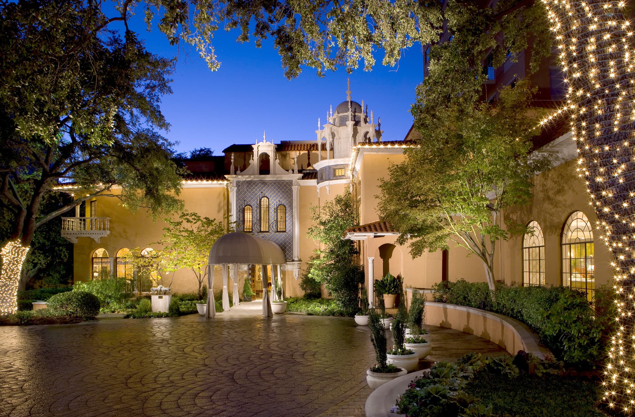 Rosewood Mansion on Turtle Creek 的桃色灰泥外墙，配有标志性的32英尺手工雕刻圆顶和修剪整齐的黄杨木花园。