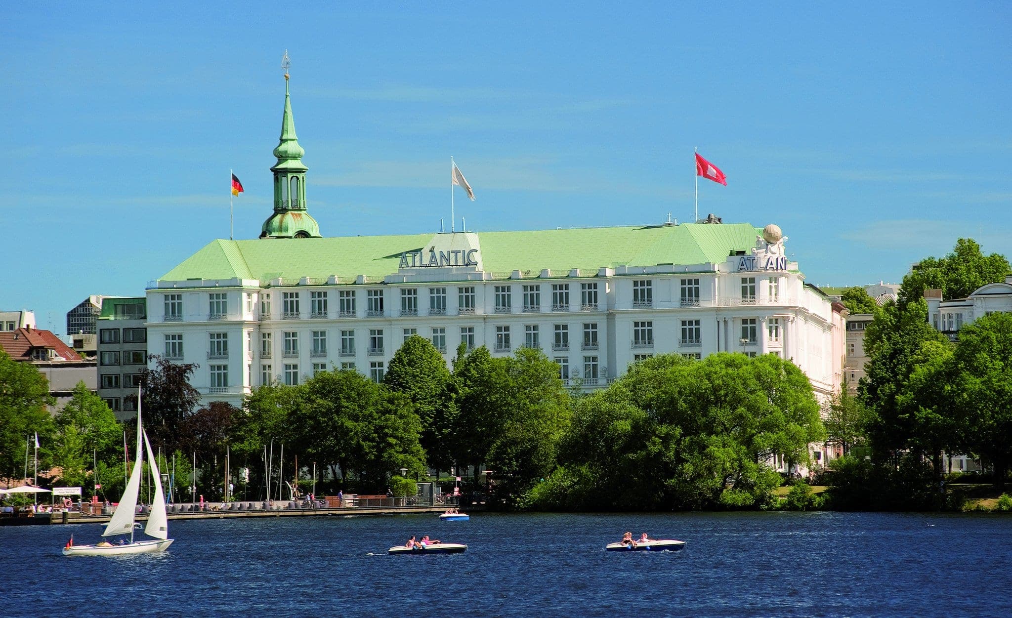 The illuminated white facade of Hotel Atlantic Hamburg reflecting on Lake Alster at twilight, with the iconic globe sculpture on the roof.