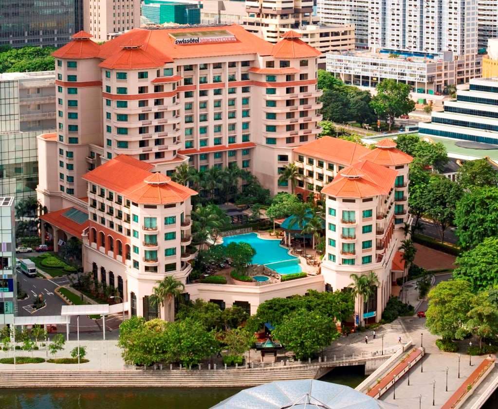 Free-form resort pool at Paradox Singapore with rock gardens and waterslides, surrounded by city skyscrapers.