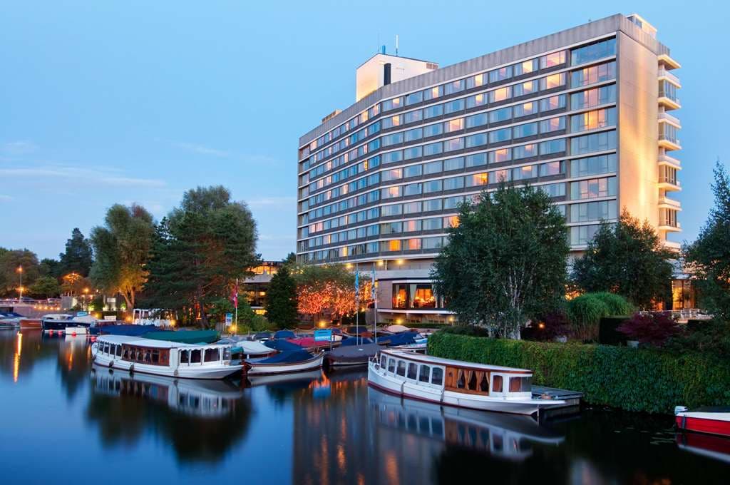 The V-shaped exterior of Hilton Amsterdam towering over the Noorder-Amstelkanaal with boats docked at its private marina.