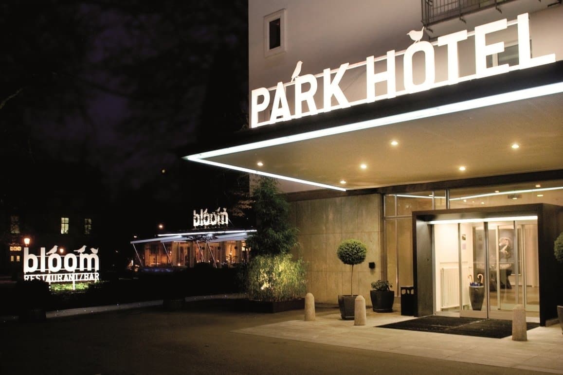 View of Restaurant Bloom's outdoor terrace at Park Hotel Winterthur surrounded by lush park greenery.