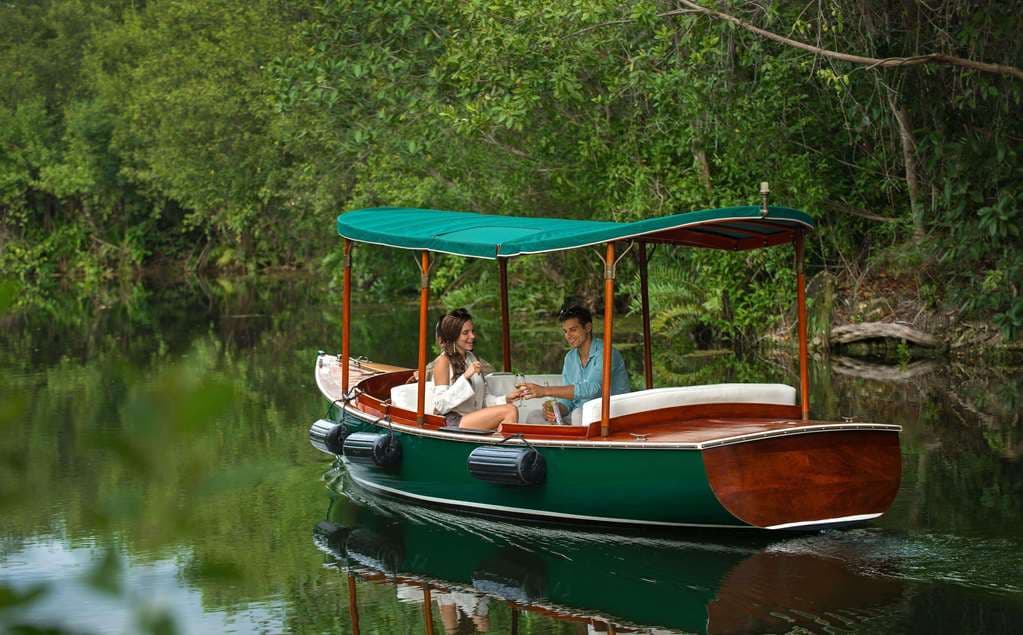 A sleek electric boat navigating the emerald mangrove canals of Fairmont Mayakoba, framed by lush jungle foliage.