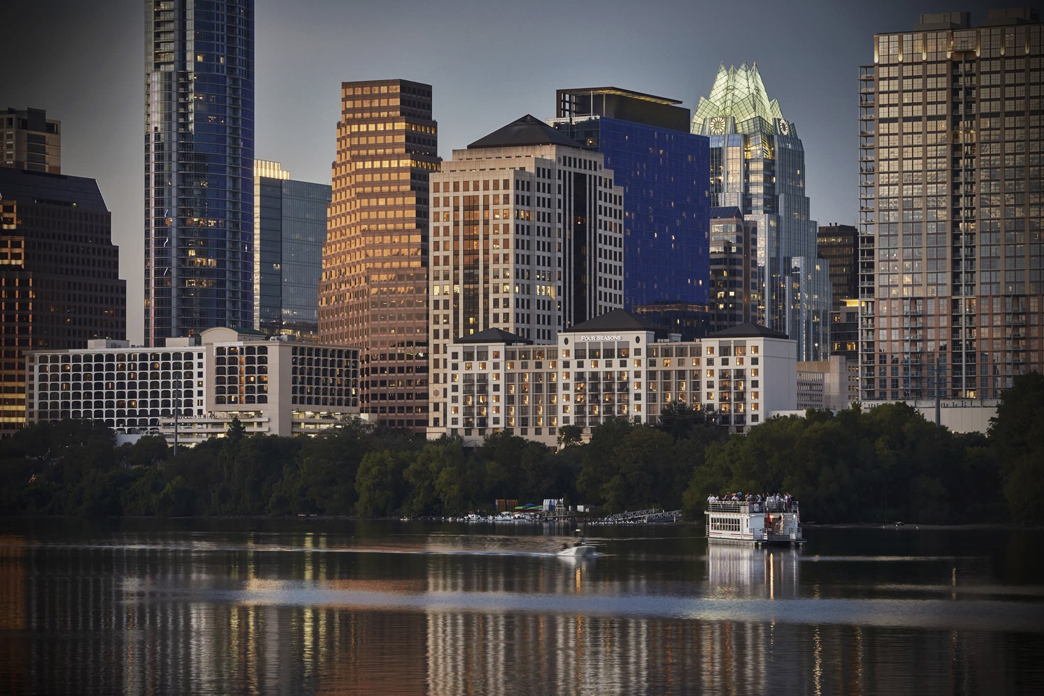 A sprawling green lawn sloping down to Lady Bird Lake with guests relaxing in hammocks and the hotel facade in the background.