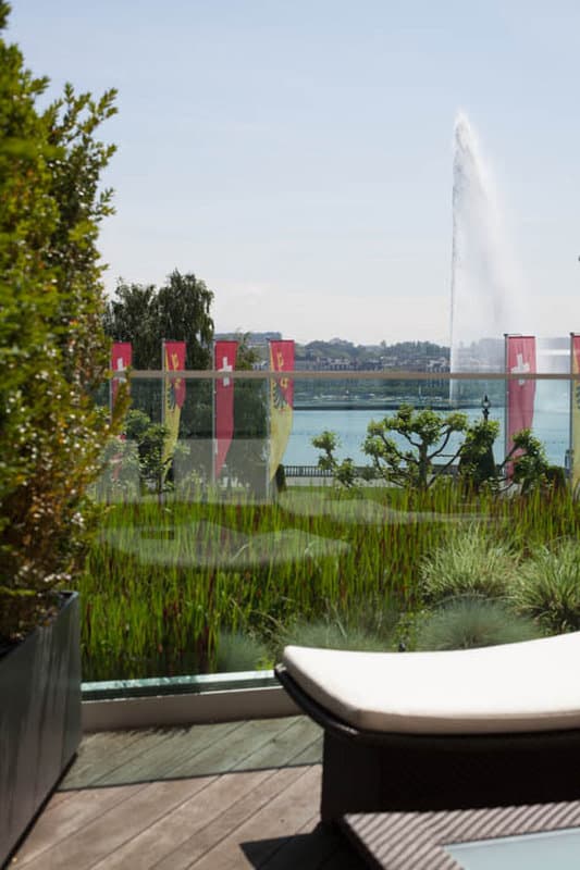 A view from the Céleste Suite balcony at Beau-Rivage Genève, featuring the Jet d'Eau fountain and Lake Geneva under a twilight sky.