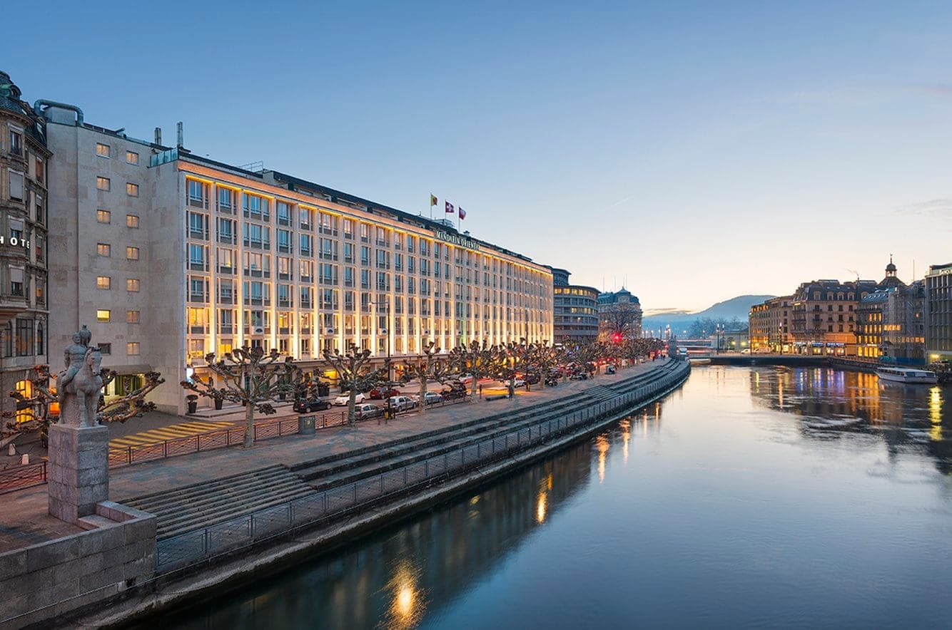 View from Mandarin Oriental Geneva suite balcony overlooking the Rhône river and Old Town at twilight.