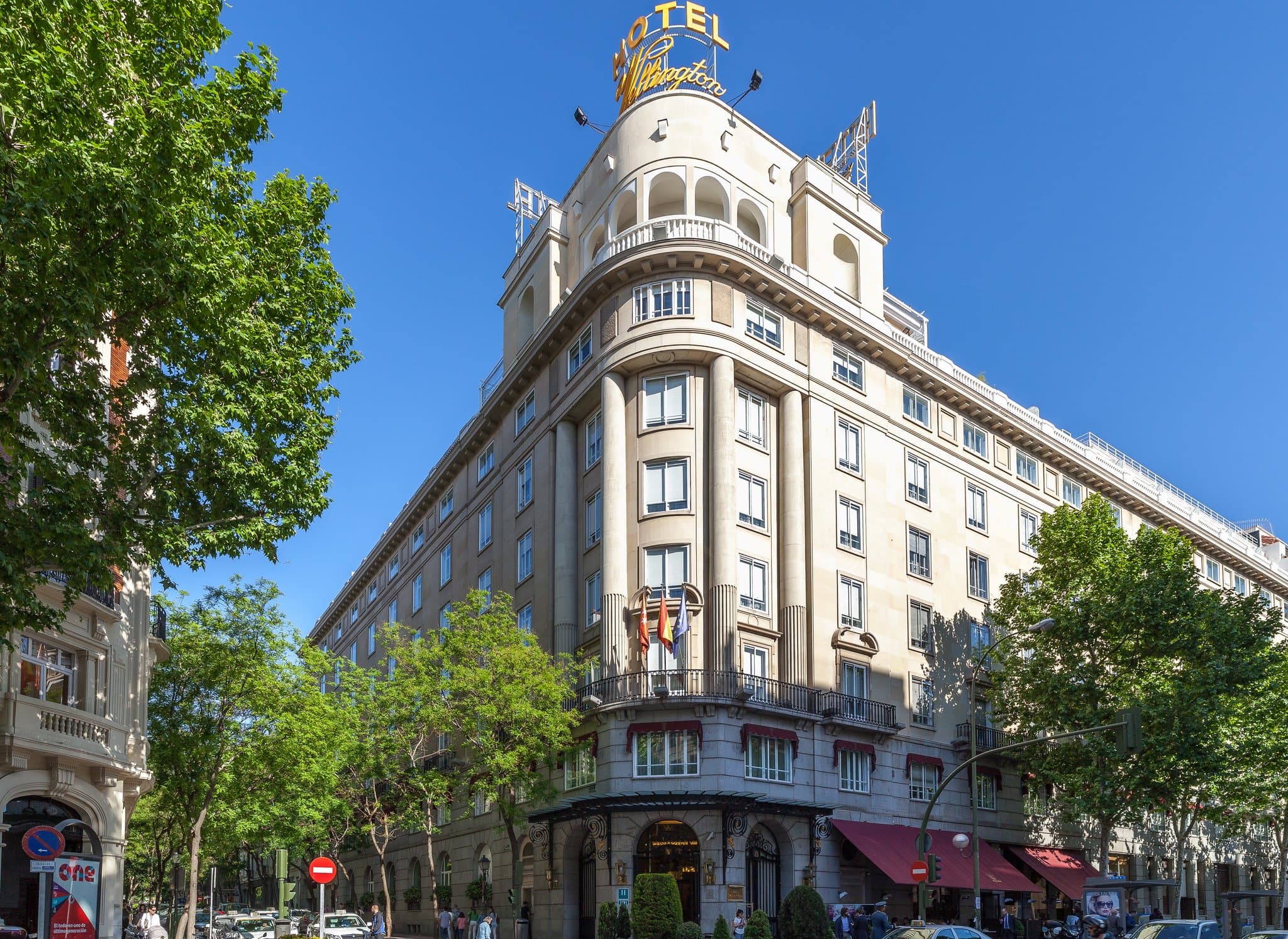 A matador in a suit of lights standing in the ornate lobby of the Wellington Hotel Madrid under a crystal chandelier.