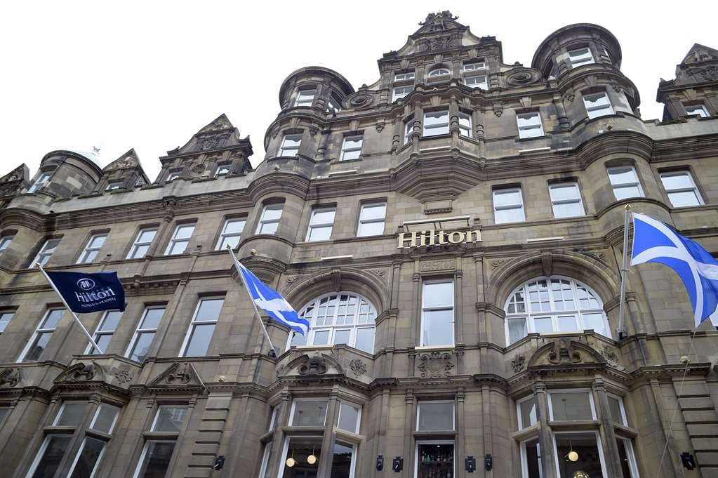 Grand lobby staircase of Hilton Edinburgh Carlton with Victorian architecture and modern lighting.