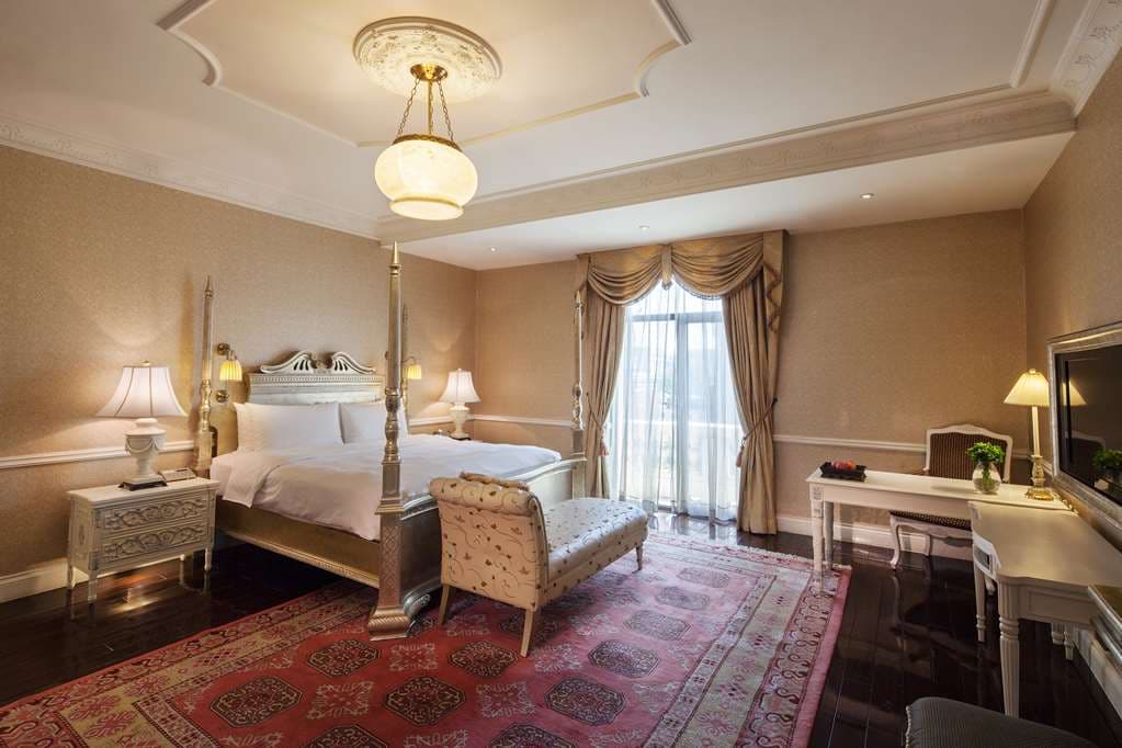 The Grand Marble Staircase of Beijing Hotel Nuo featuring a plush red carpet and ornate iron railings under warm chandelier light.