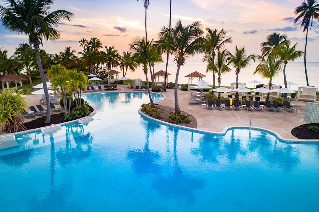 Sprawling lagoon-style pool at Hyatt Regency Grand Reserve Puerto Rico with floating Bali beds and El Yunque rainforest mountains in the background.