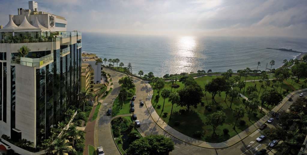 A guest sipping a Pisco Sour by the rooftop infinity pool at Miraflores Park, overlooking the Pacific Ocean and Lima's coastline.