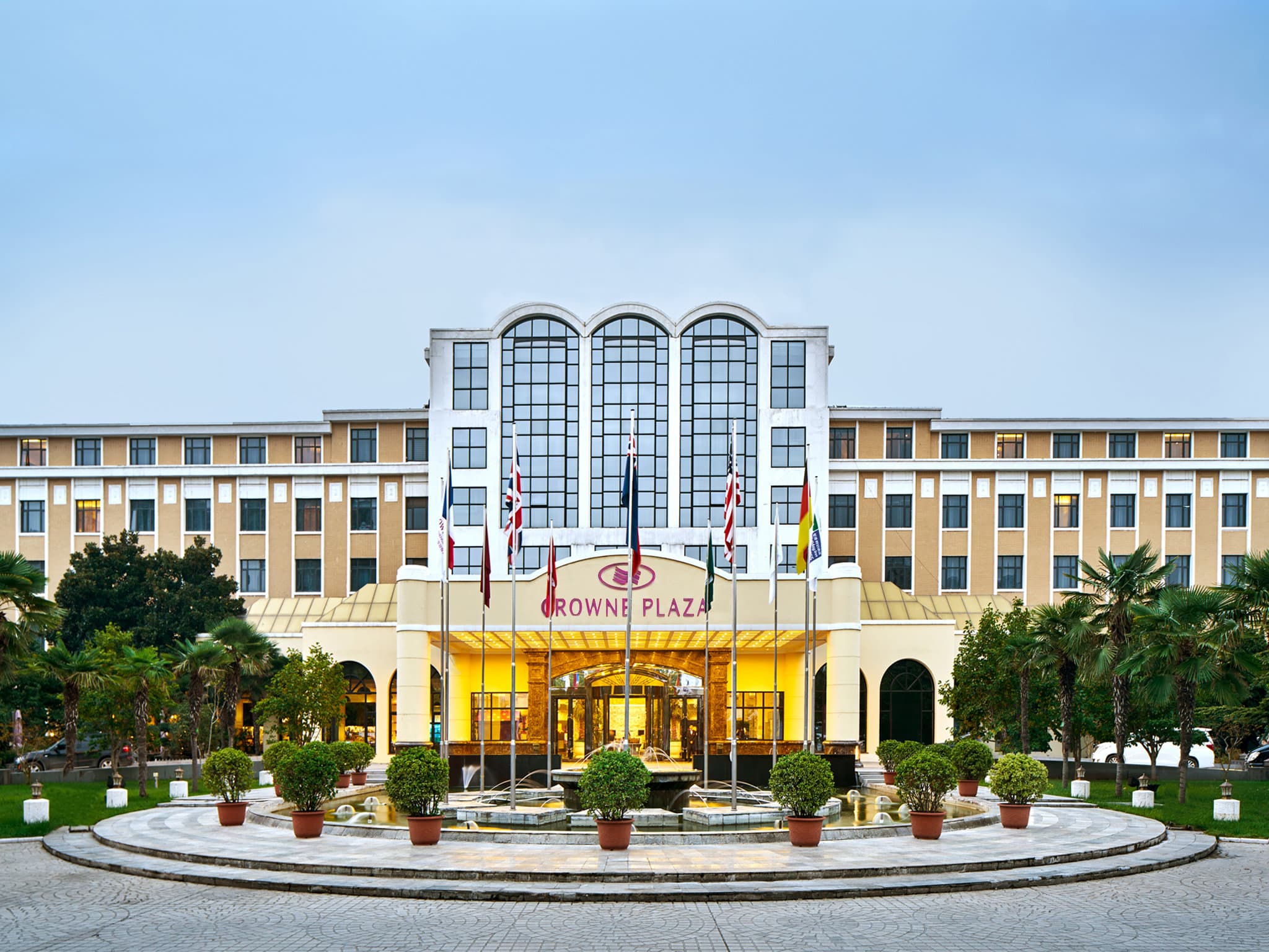 A wide shot of the Crowne Plaza Zhengzhou's historic 1950s facade, framed by the lush greenery of its massive private gardens.