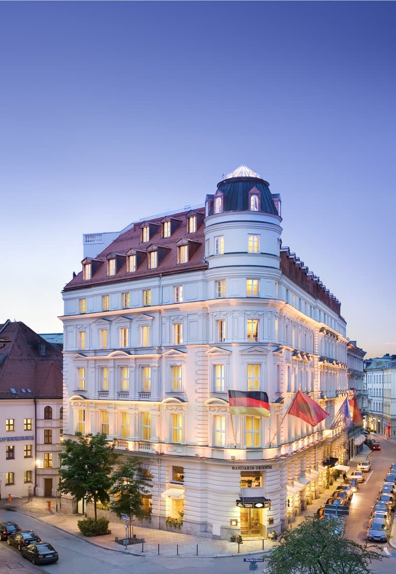 Rooftop infinity pool at Mandarin Oriental Munich with guests lounging on Roche Bobois furniture, overlooking the Munich skyline and distant Alps.