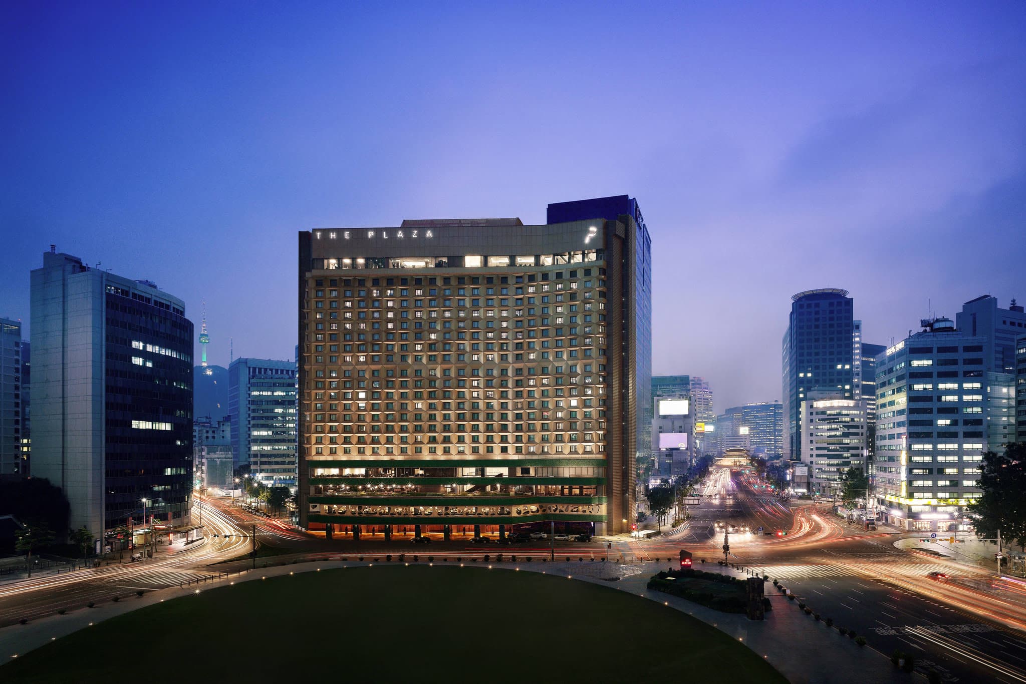 View from THE PLAZA Seoul suite looking out over the illuminated Seoul City Hall and Deoksugung Palace at twilight.
