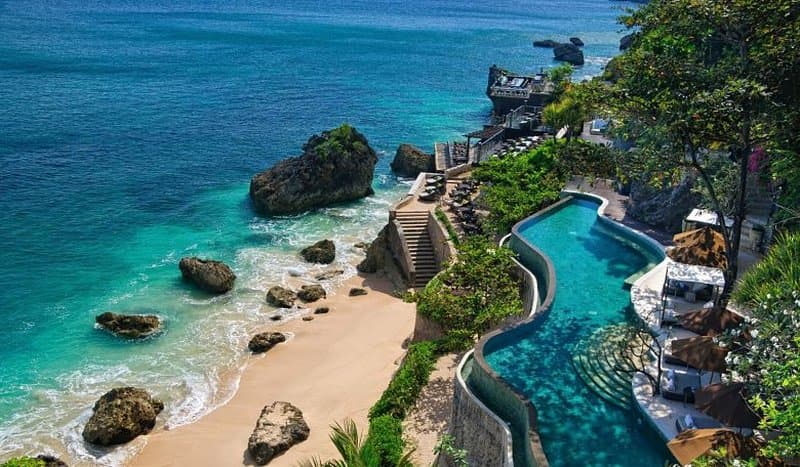Sunset view of the Rock Bar at AYANA Resort Bali, perched on natural rocks above crashing waves.