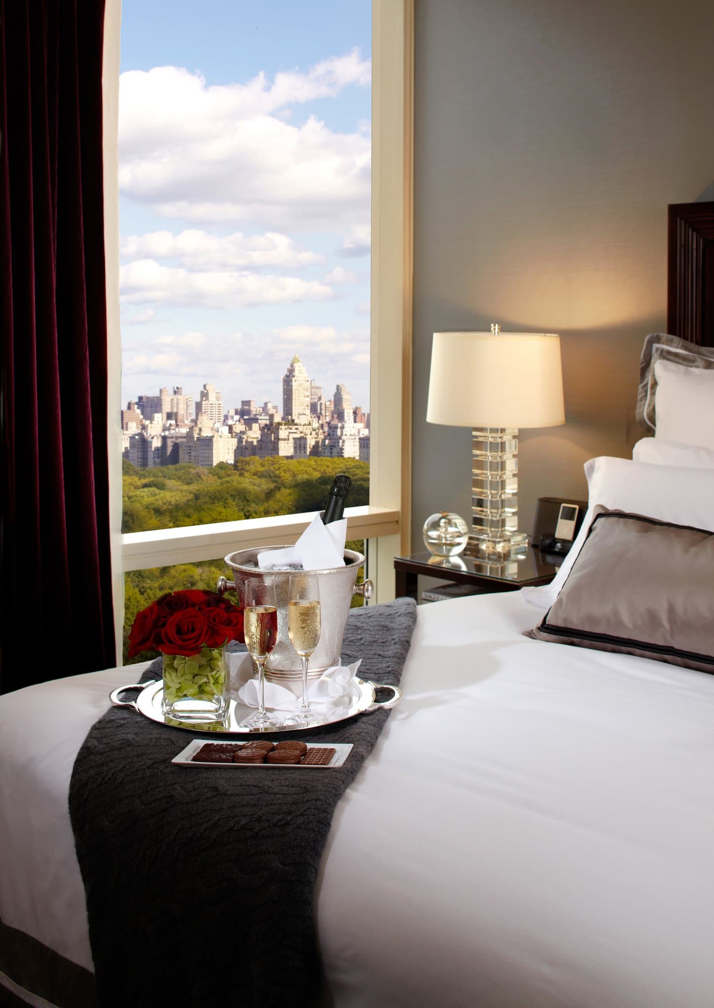 A guest in a plush robe sitting on a deep window ledge at Trump International Hotel, silhouetted against a panoramic view of Central Park's greenery and the Manhattan skyline.