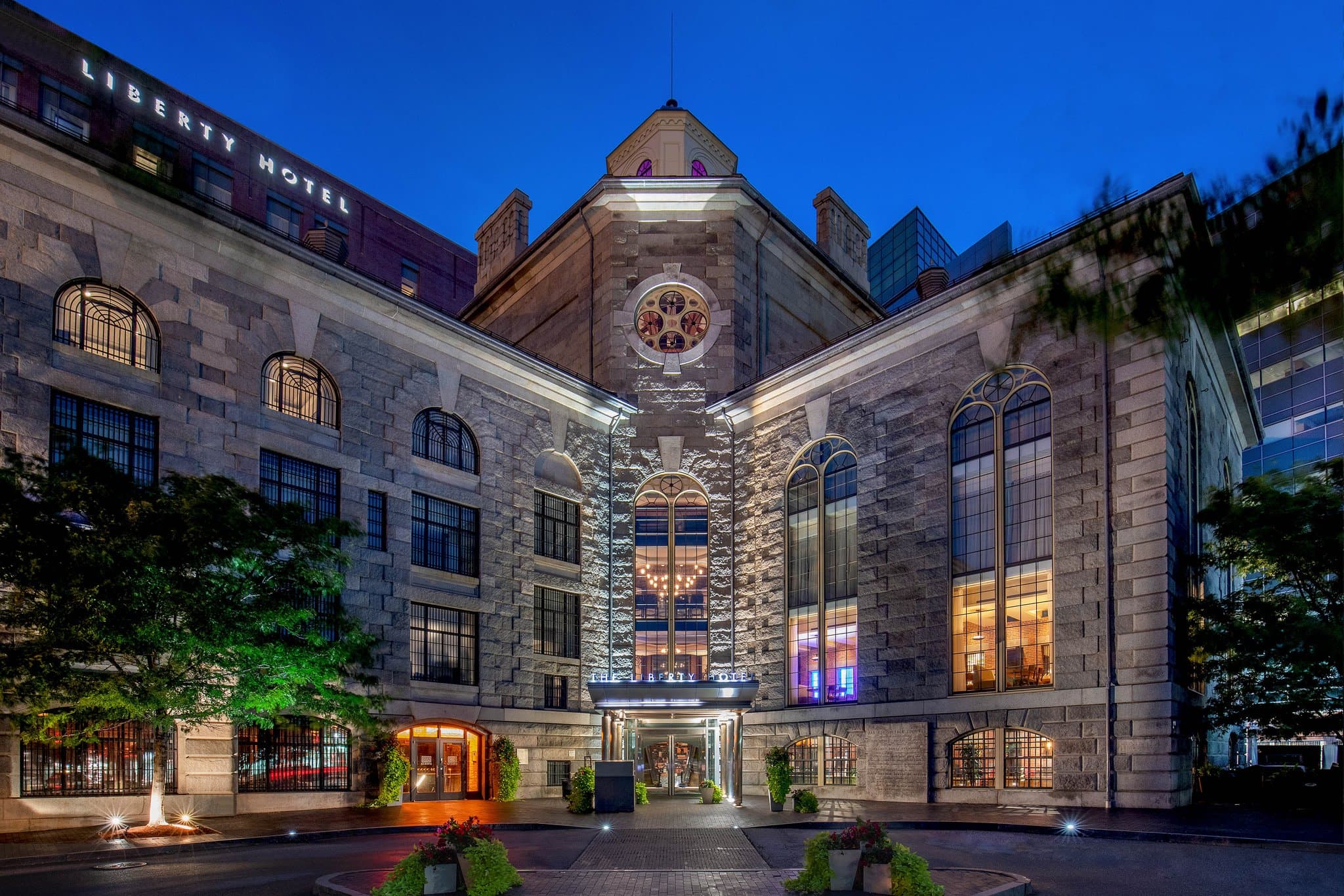 The Liberty Hotel's soaring 90-foot rotunda lobby featuring original jail catwalks, circular chandeliers, and guests dining at the CLINK. restaurant.