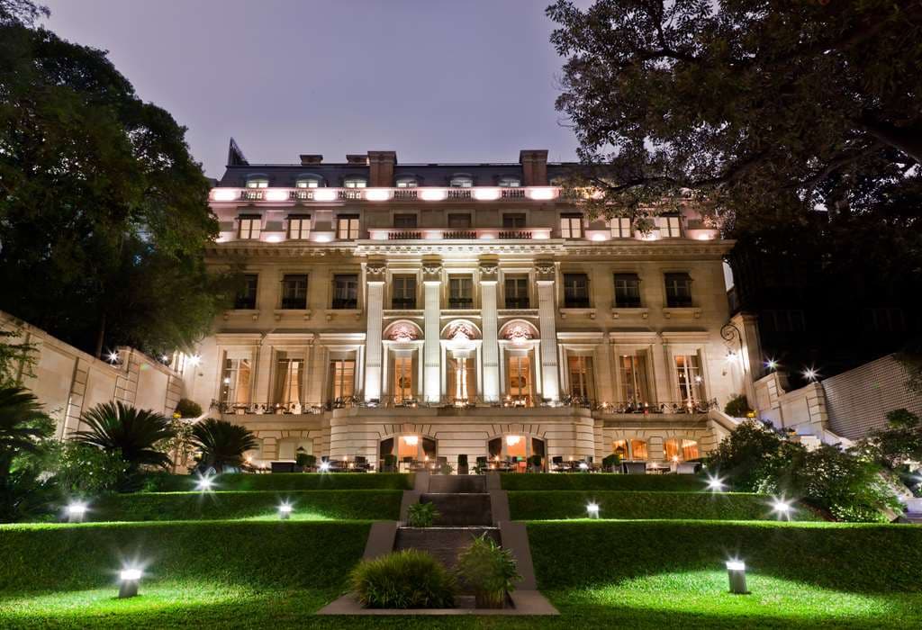 The neoclassical facade of Palacio Duhau illuminated at twilight, viewed from the terraced Secret Garden.