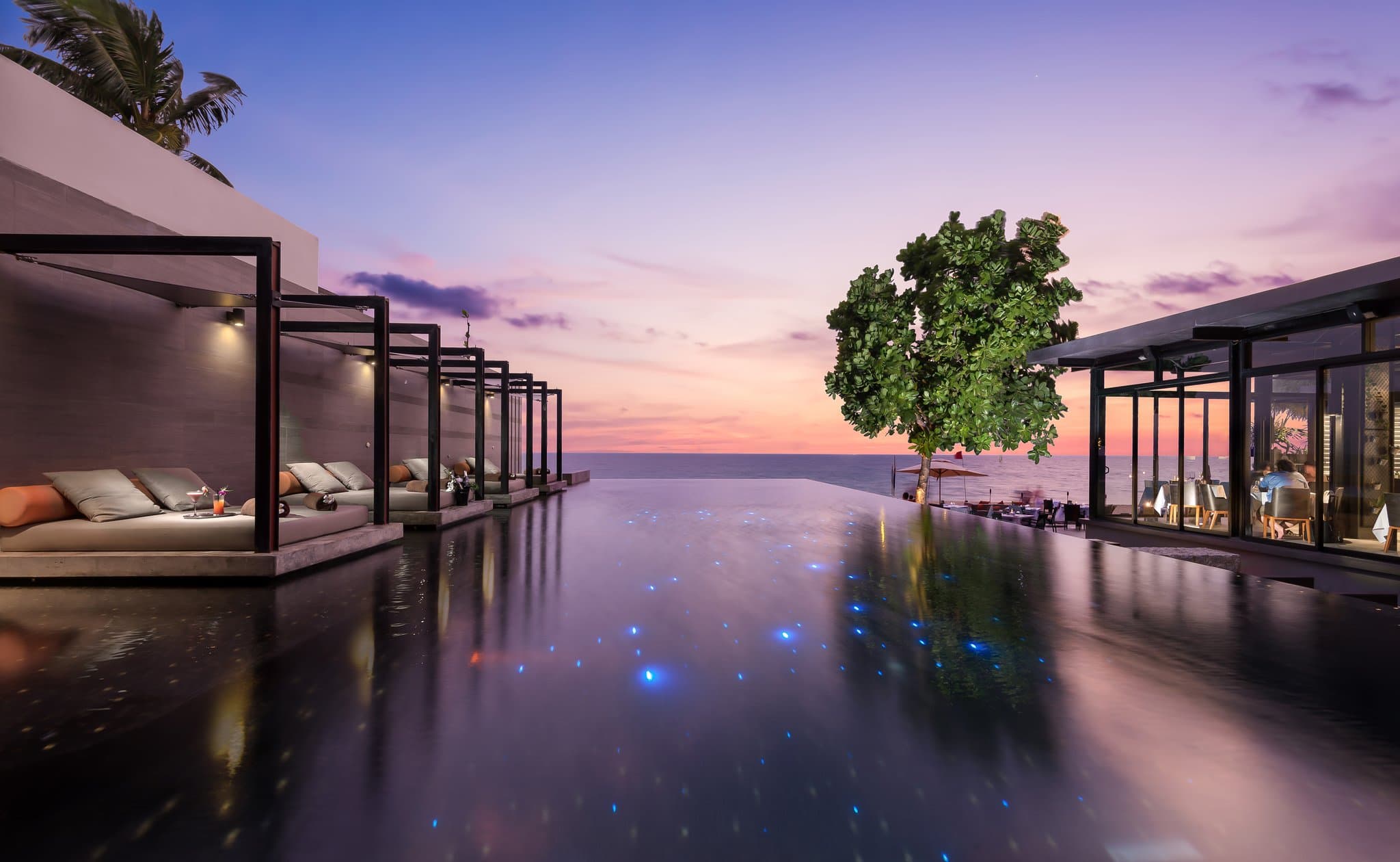 View from an Aleenta Pool Villa looking out to the Andaman Sea at sunset, featuring a private infinity pool and timber decking.