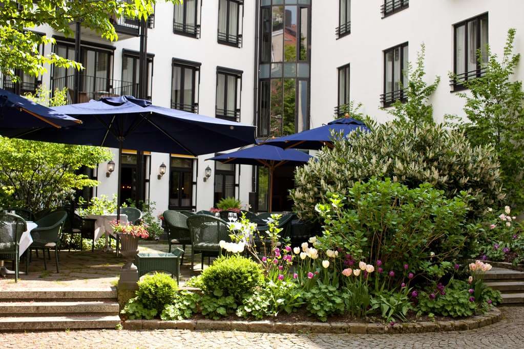 Elegant courtyard garden at Hotel München Palace with guests dining at tables with white linens under large parasols.