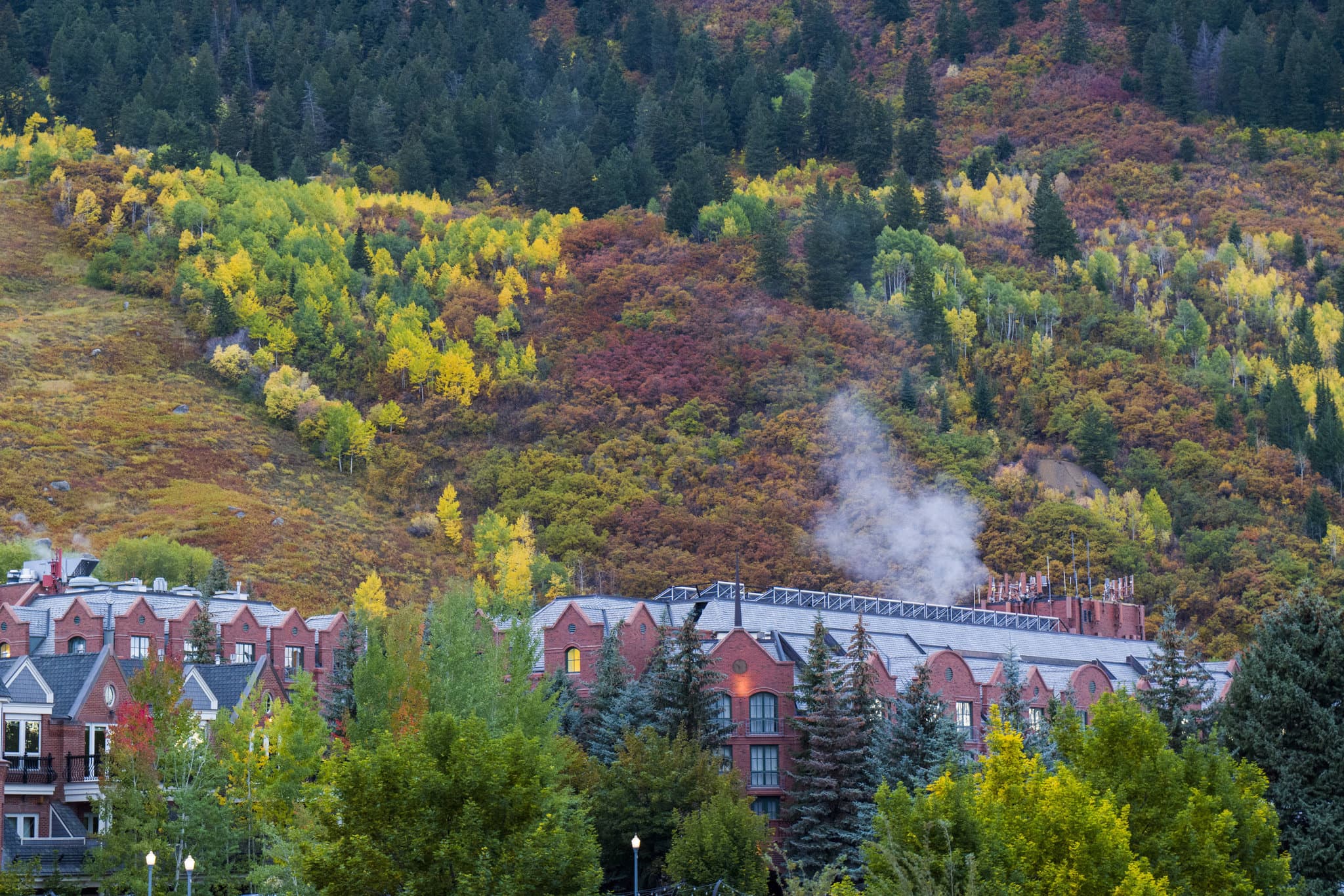 The red brick facade of The St. Regis Aspen Resort framing the heated outdoor pool, with steam rising against the snowy backdrop of Aspen Mountain.