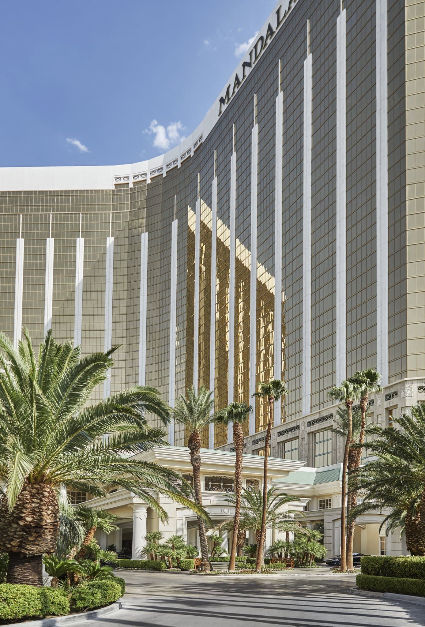 A serene, private pool area lined with white cabanas and lush palm trees, with the golden Mandalay Bay tower reflecting the sun in the background.