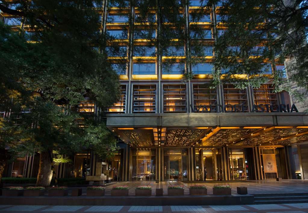 The Waldorf Astoria Beijing's bronze lattice facade glowing at dusk, contrasting with traditional grey-brick hutong courtyards.