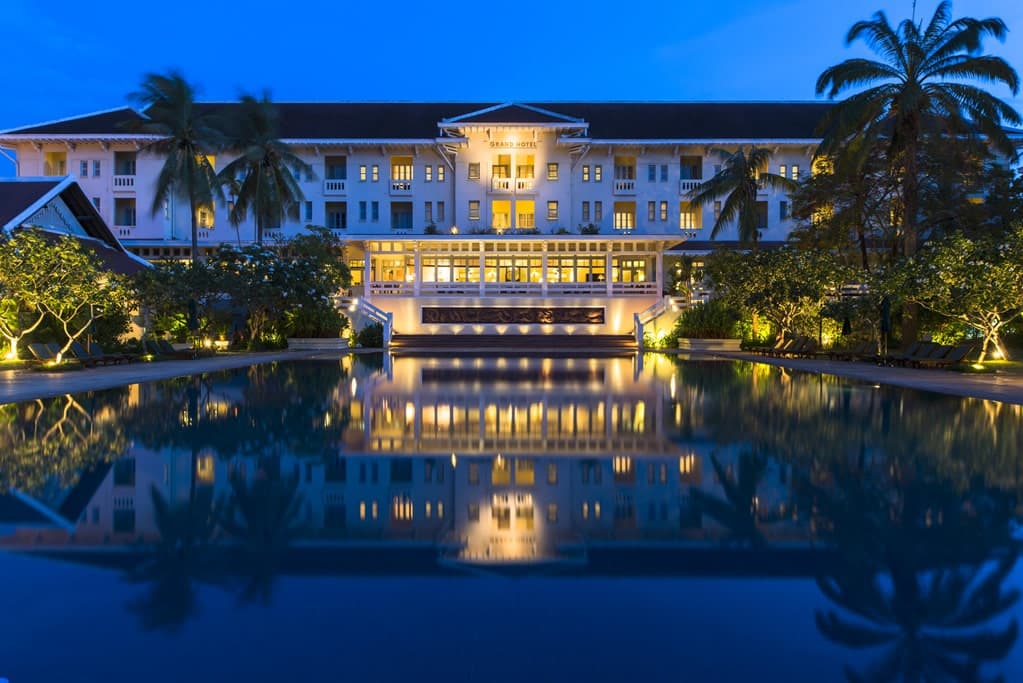 The iconic 35-meter lap pool at Raffles Grand Hotel d'Angkor, inspired by ancient Royal Baths, flanked by white colonial architecture and palm trees.