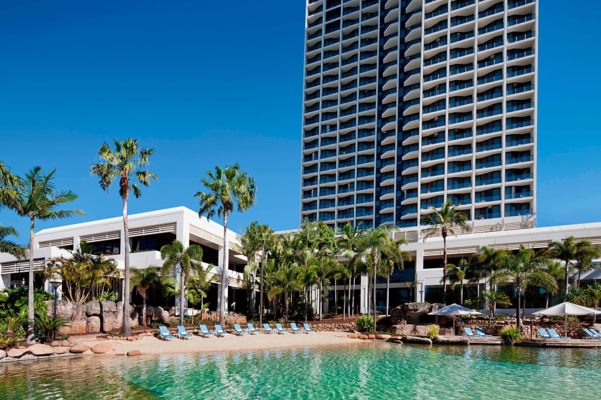 A vibrant saltwater lagoon pool at JW Marriott Gold Coast with a waterfall and tropical landscaping, filled with swimmers and colorful fish.