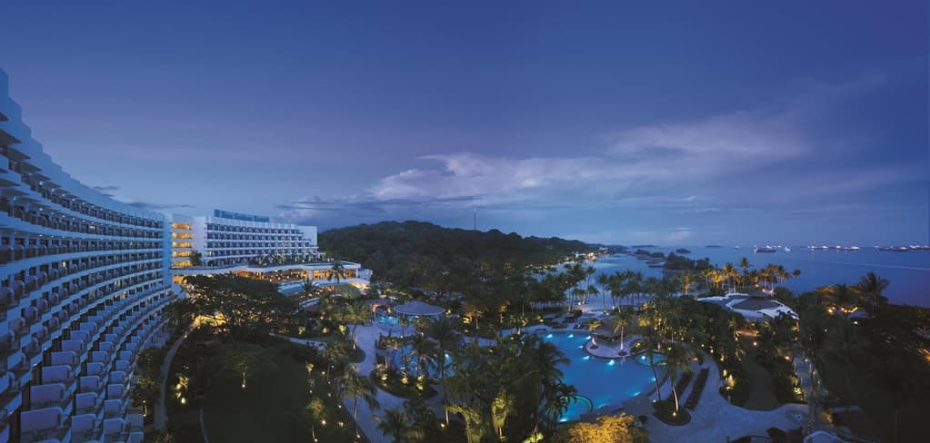 View from a Shangri-La Rasa Sentosa balcony looking out over the free-form pool and slides towards the open sea at sunset.