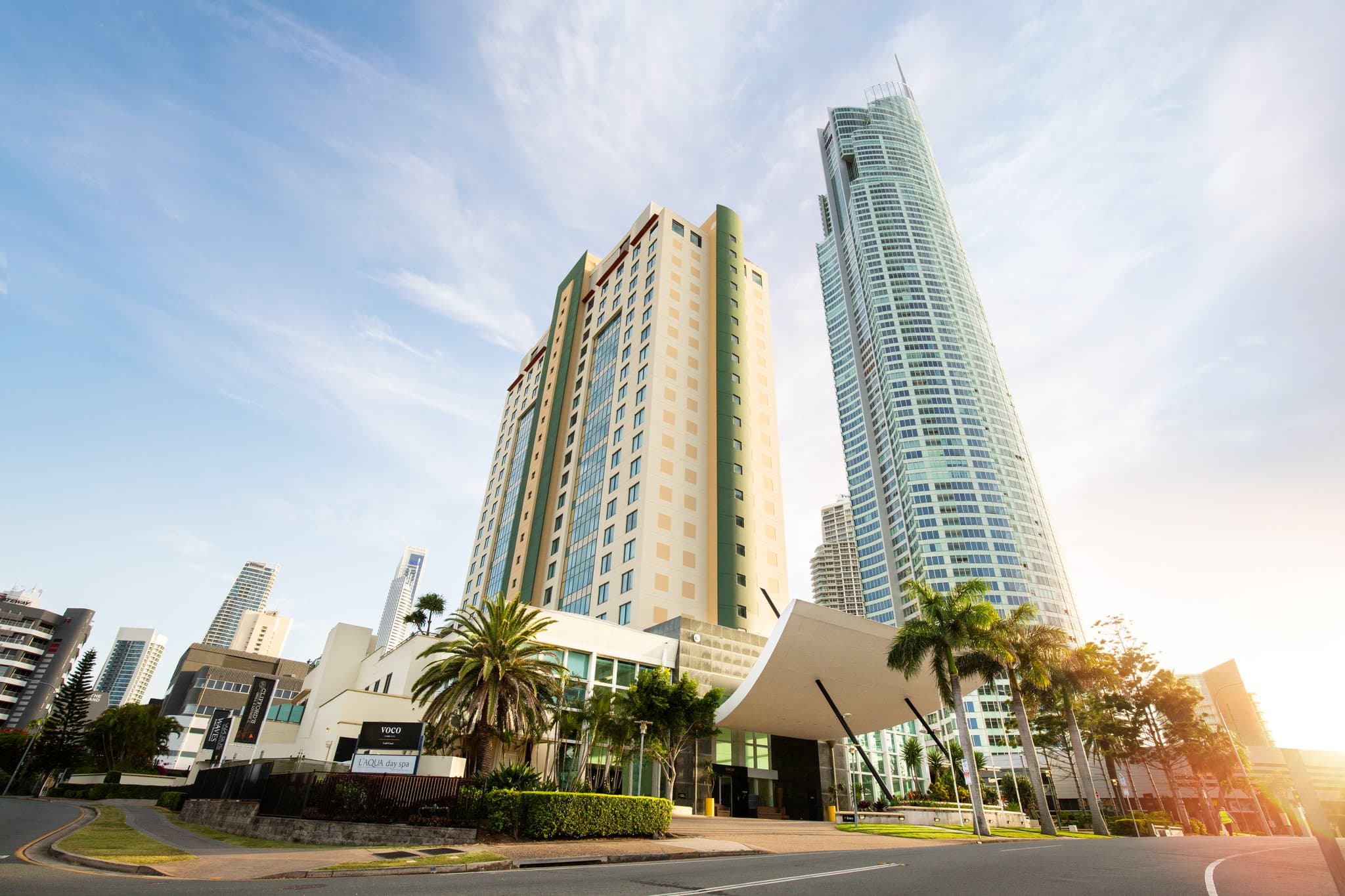 A vibrant poolside scene at voco Gold Coast featuring yellow umbrellas and the Q1 building in the background.