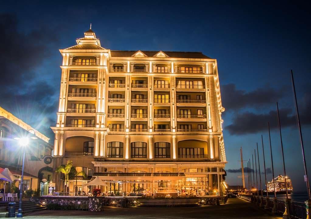 View of Labourdonnais Waterfront Hotel facade at twilight with lit marina boats in foreground.