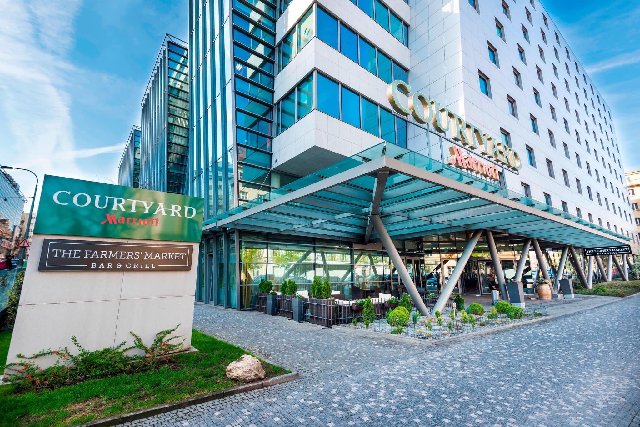 The lobby of Courtyard Prague City featuring a warm, stone-clad fireplace and modern seating, contrasting with the vibrant 'The Market' wall in the background.