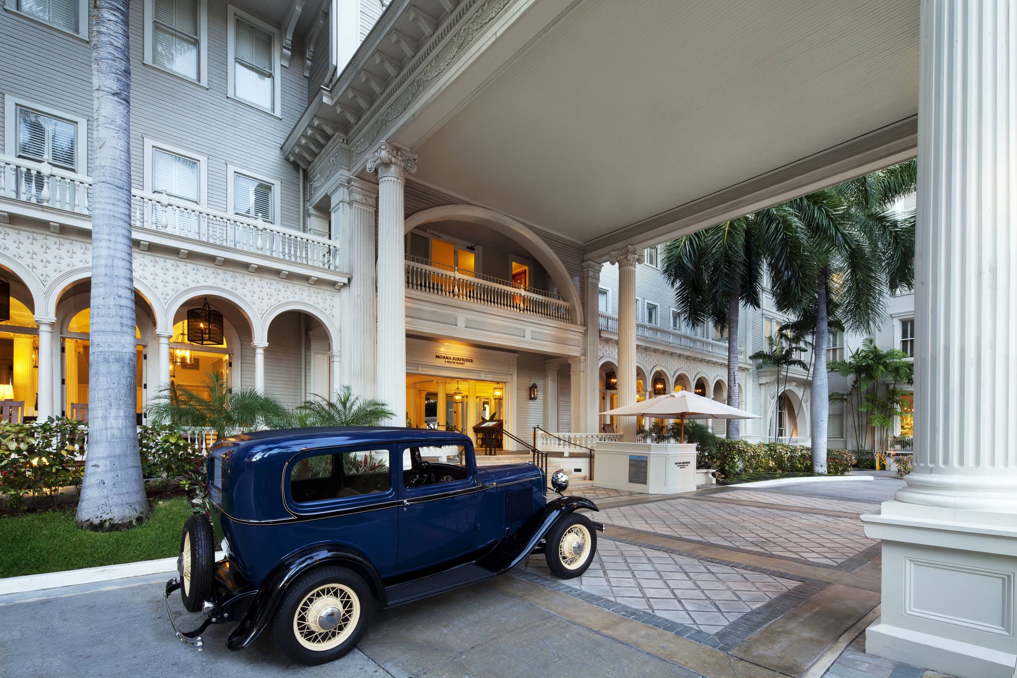 Victorian architecture of Moana Surfrider lobby with guests relaxing in rocking chairs on the veranda.